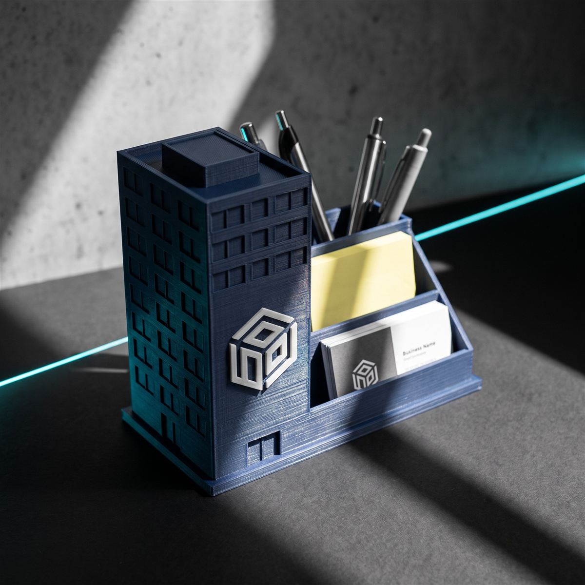 Organizador de mesa impresso em 3D em formato de prédio azul-marinho, com canetas, bloco de notas e cartões